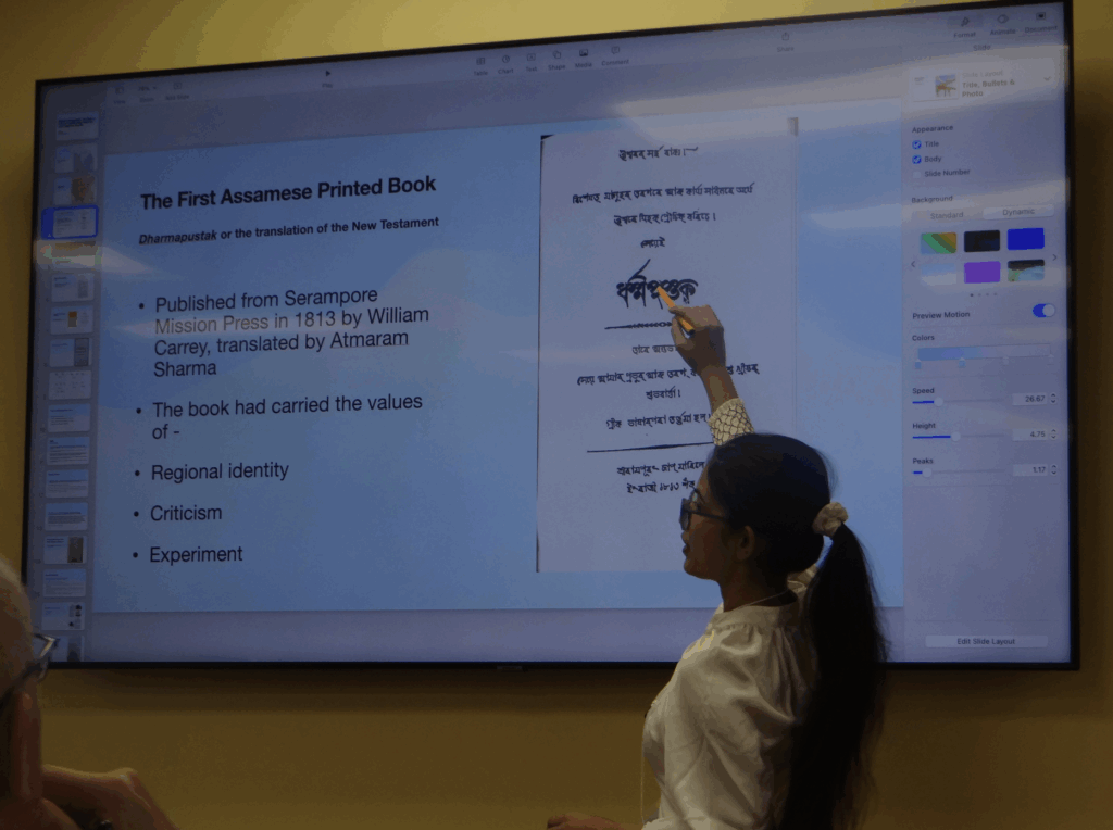 Photo of Simi Nath showcasing a cover page and transcription for "The First Assamese Printed Book."