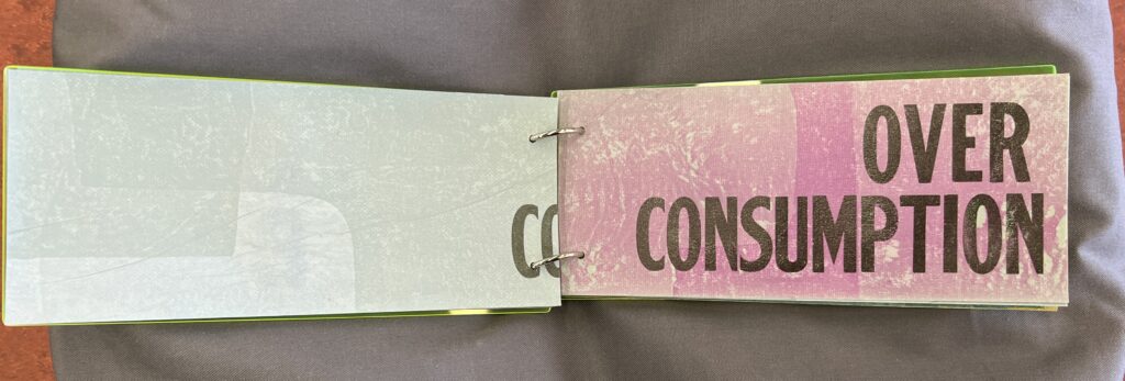 The book is open to the page “Overconsumption,” with text screenprinted on the recto. On the verso, the letters “CO” trail into the gutter.