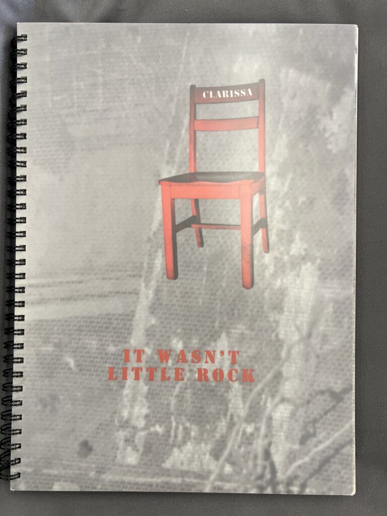 View of the spiral bound front cover of ‘It Wasn’t Little Rock.’ The title text is printed in red on a background of a blurry black & white archival photo. Above the text, a red simple chair is emblazoned with the name “Clarissa” in white. 
